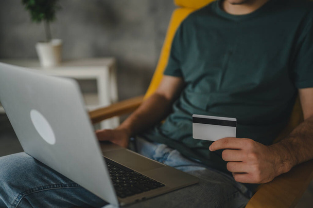 Jeden teenager mladý muž kavkazský muž sedět doma používat kreditní karty a notebook nakupování on-line používat internet pro online nákup aktivní moderní e-bankovnictví používat notebook - Fotografie, Obrázek