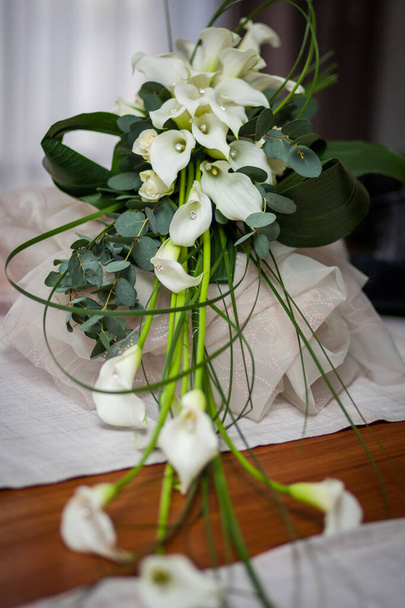 Elegantemente adagiato su una superficie lignea, questo bouquet nuziale presenta una cascata di calle bianche, dalle forme eleganti e graziose che creano un'estetica fluida. Accentati con rametti di eucalipto e - Foto, immagini