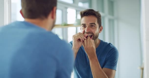 Refleksja, mężczyzna w łazience z nicią dentystyczną i poranną rutyną mycia zębów i samoopieki. pielęgnacja, oczyszczanie ust i nici dentystyczne, mężczyzna w lustrze z uśmiechem i szykuje się ze świeżą twarzą - Materiał filmowy, wideo
