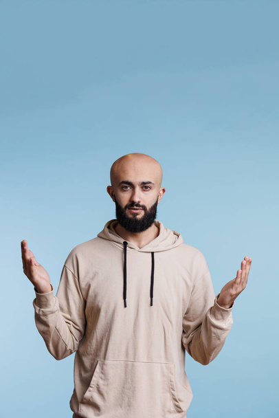 Arab man praying in spiritual gesture with raised hands while looking at camera with calm facial expression. Young person pleading and asking for blessing with open arms studio portrait - Photo, Image