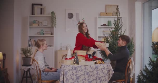 休暇中に自宅で男性と女性の友人にクリスマスプレゼントを贈る若い女性 - 映像、動画
