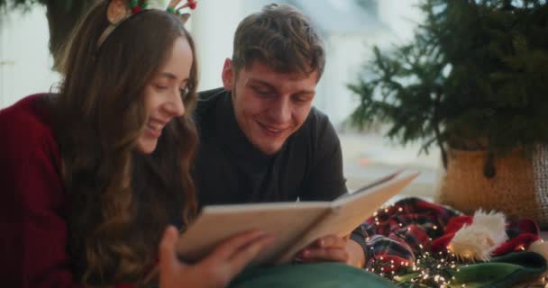 Ευτυχισμένο ετεροφυλόφιλο ζευγάρι βλέποντας φωτογραφικό άλμπουμ μαζί στο σπίτι κατά τη διάρκεια των διακοπών των Χριστουγέννων - Πλάνα, βίντεο
