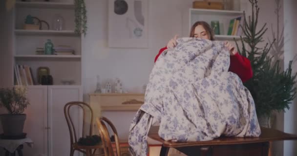 Jovem mulher colocando toalha de mesa na mesa, enquanto em pé na sala de estar em casa - Filmagem, Vídeo