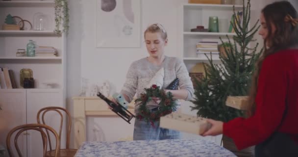 Νέοι γυναίκες και άνδρες φίλοι τοποθέτηση χριστουγεννιάτικη διακόσμηση στο τραπέζι στο σπίτι κατά τη διάρκεια των διακοπών - Πλάνα, βίντεο