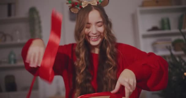 Ευτυχισμένη νεαρή γυναίκα αφαιρώντας κορδέλα από τα κουτιά δώρο Χριστουγέννων στο σπίτι - Πλάνα, βίντεο
