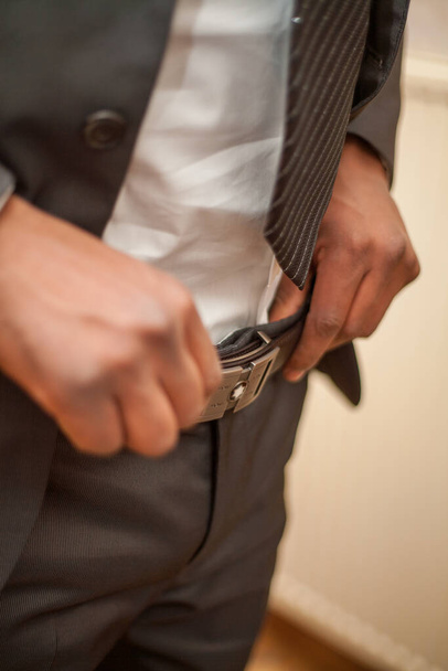 A detailed view of a mans midsection as he secures his belt buckle, preparing to present himself in his best light. The close-up shot emphasizes the interaction between the sleek belt and the well - Photo, Image