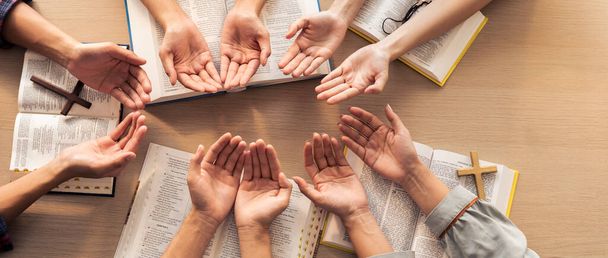 Rajattu kuva monimuotoisuuden ihmiset käsi rukoilee yhdessä puukirkossa Raamatun kirja. Ryhmä uskovia pitää toisiaan kädestä uskollisesti. Käsitys toivosta, uskonnosta, uskosta, Jumalan siunauksesta. Kasvaminen. - Valokuva, kuva