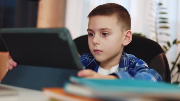 Enfant masculin caucasien vêtu de vêtements décontractés utilisant une tablette numérique dans un étui noir pour faire ses devoirs. Enfant concentré avec une expression concentrée se comportant de manière responsable sur l'apprentissage en ligne à l'aide d'un gadget moderne. - Séquence, vidéo