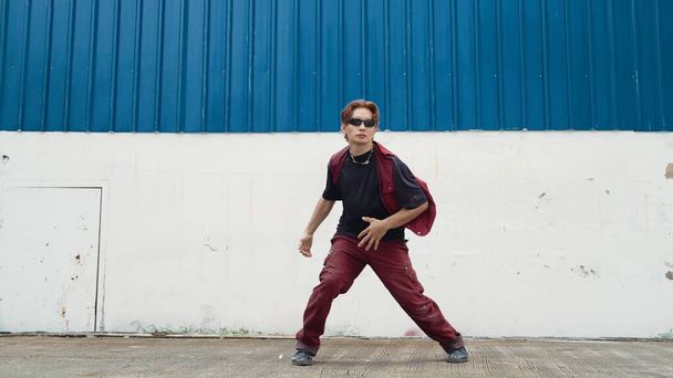 Przystojny uliczny tancerz ćwiczący break dance na białym podwórku. Sport człowiek noszenia stylu hip hop podczas poruszania się kroki do muzyki na ulicy z niebieskim tle. Sport na świeżym powietrzu 2024. Endeavor. - Zdjęcie, obraz