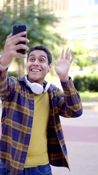 Κατακόρυφο βίντεο αργής κίνησης ενός ευτυχισμένου Λατίνου μαθητή που χαιρετάει κατά τη διάρκεια βιντεοκλήσης στην πανεπιστημιούπολη - Πλάνα, βίντεο