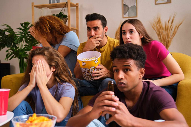 Gruppe von Freunden, die sich einen Horrorfilm ansehen, leiden, die Augen verdecken, interessiert starren. - Foto, Bild
