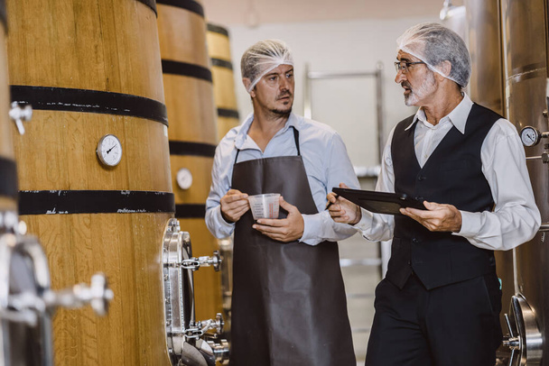 現代の大型ワイナリー工場アルコール飲料業界の品質管理と発酵モニターヴィンテージカラートーンで働くワインメーカーの専門家 - 写真・画像