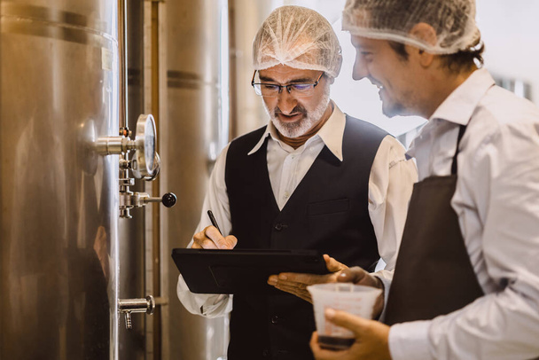 現代の大型ワイナリー工場アルコール飲料業界の品質管理と発酵モニターヴィンテージカラートーンで働くワインメーカーの専門家 - 写真・画像