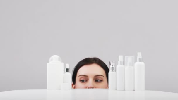 Beautiful young caucasian woman with perfect healthy skin proposing a product. Cosmetic bottles with a white label. Beauty blog, salon concept, minimalism brand packaging mockup - Footage, Video
