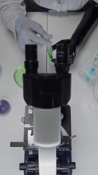 Protez kol şişesiyle tanınmayan bir kadının ellerinin dikey görüntüsü. Petri kabına ekilmiş hücrelerle yeşilimsi substrat dökerek biyokimya laboratuvarında çalışma yapıyor. - Video, Çekim