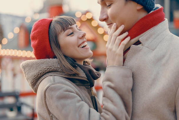 Capturando la alegría, una joven pareja comparte una risa, su afecto palpable en el contexto de un vibrante mercado de Navidad - Foto, imagen