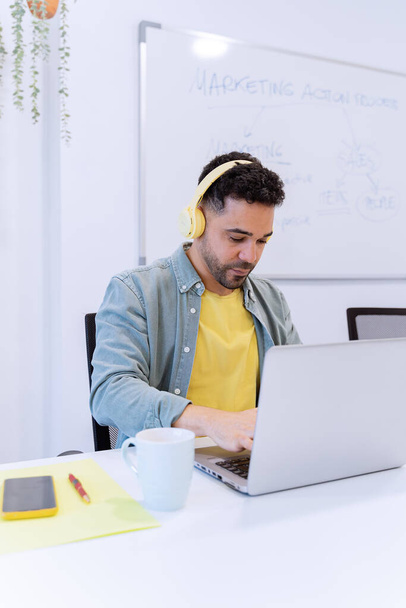 Hombre usando auriculares mientras trabaja con un portátil en la oficina. Concepto de negocio y tecnología. - Foto, Imagen