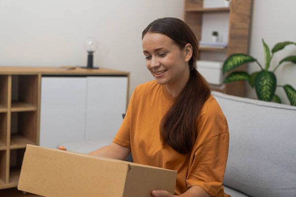 Female unpacking huge cardboard box from internet store feeling excited of receiving parcel young woman with ponytail rejoices at receiving package with goods at home - Photo, Image