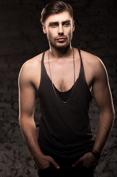 handsome muscular man in a black t-shirt standing near the wall - Foto, afbeelding