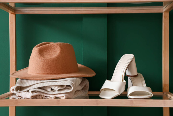 Regal mit eleganten weißen Absatzschuhen, Mütze und Schal in der Nähe der grünen Wand in der Boutique, Nahaufnahme - Foto, Bild