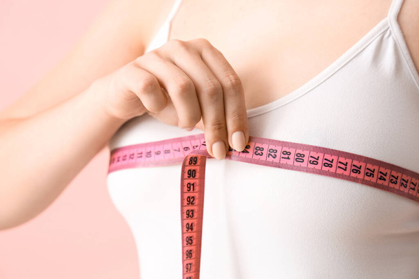 Nainen mittaamassa rintojaan vaaleanpunaisella pohjalla, lähikuva. Käsitys plastiikkakirurgia - Valokuva, kuva