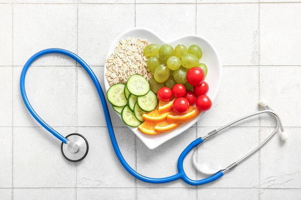 Plate with fresh healthy products and stethoscope on light tile background. Diet concept - Photo, Image