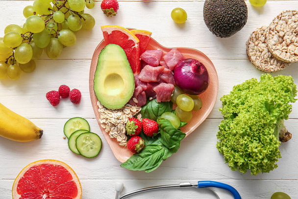 Тарелка со свежими здоровыми продуктами и стетоскопом на светлом деревянном фоне. Концепция питания - Фото, изображение