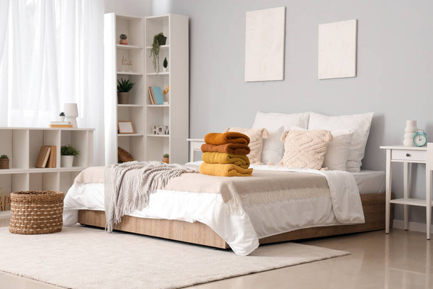 Stack of warm knitted sweaters on bed in modern bedroom - Photo, Image