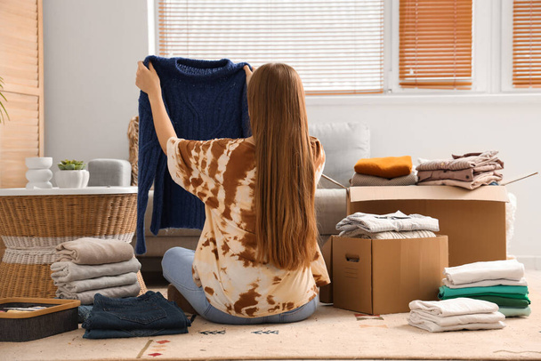 Junge Frau packt Kleidung im Wohnzimmer in Karton - Foto, Bild