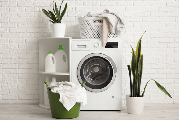 Waschmaschine mit schmutziger Wäsche und grünen Zimmerpflanzen in der Nähe weißer Ziegelwände - Foto, Bild