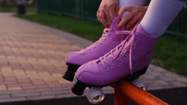 meisje strikken veters op vintage rolschaatsen, close-up van de handen, roze rolschaatsen op groen gras achtergrond - Video