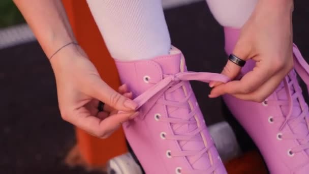 menina amarrando laços em patins de rolo vintage, close-up de mãos, patins de rolo rosa no fundo de grama verde - Filmagem, Vídeo