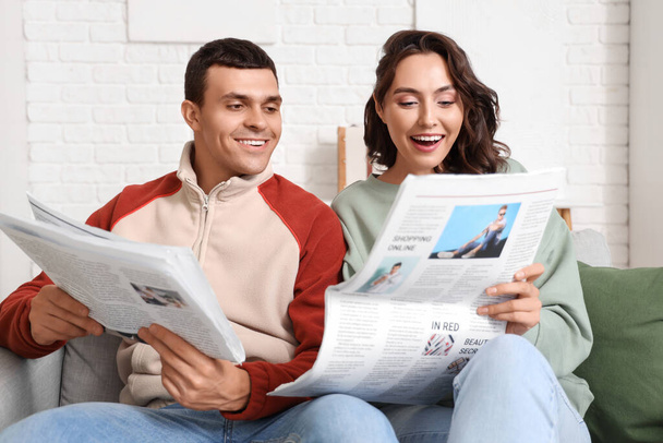 Νεαρό ζευγάρι με εφημερίδες στο σπίτι - Φωτογραφία, εικόνα