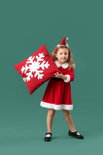 Linda niña en traje de Santa Claus con hermoso cojín de Navidad en el fondo de color - Foto, Imagen