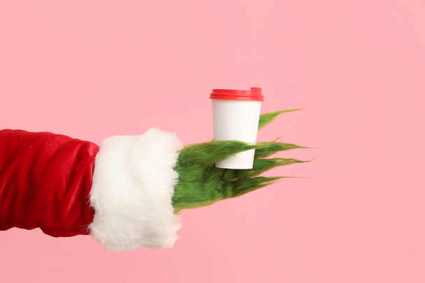 Zelená chlupatá ruka stvoření v kostýmu Santa s kávou na růžovém pozadí - Fotografie, Obrázek