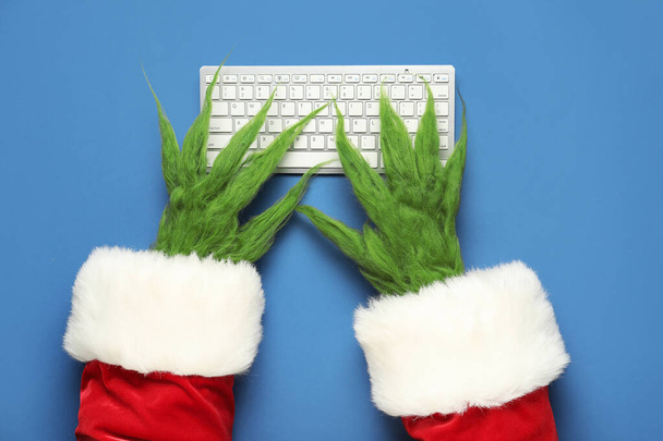 Verde mãos peludas de criatura no traje de Santa com teclado no fundo azul - Foto, Imagem