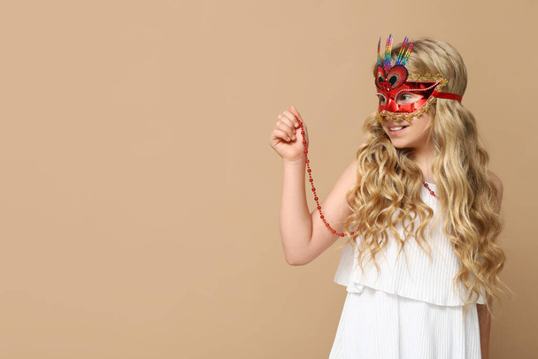Αστείο κοριτσάκι που φοράει μάσκα καρναβαλιού σε μπεζ φόντο - Φωτογραφία, εικόνα