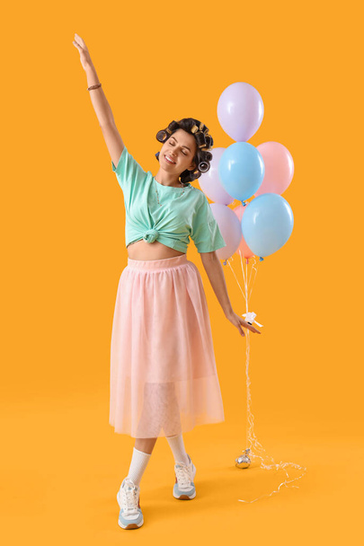 Young woman with hair curlers and balloons on yellow background - Photo, Image