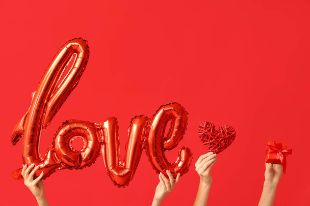 愛の言葉,装飾的なハート,赤い背景のギフトボックスの形をしたエアバルーンを持つ女性の手. バレンタインデーのお祝い - 写真・画像