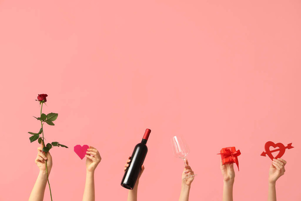 Manos femeninas con corazones, rosa roja, caja de regalo, copa y botella de vino sobre fondo rosa. Celebración de San Valentín - Foto, imagen