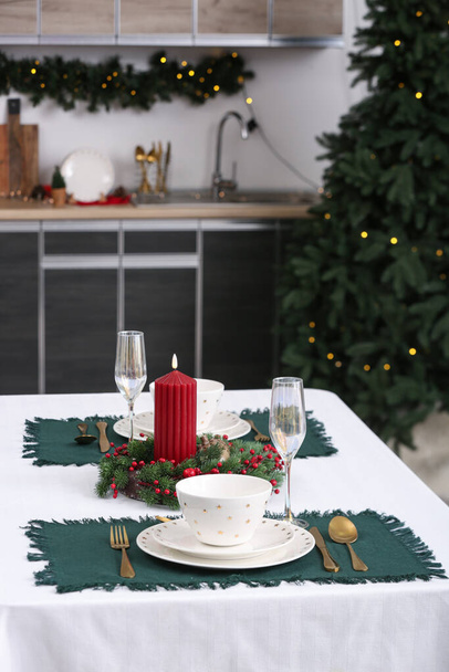 сервировка стола с рождественским венком и горящей свечой на кухне, крупным планом - Фото, изображение