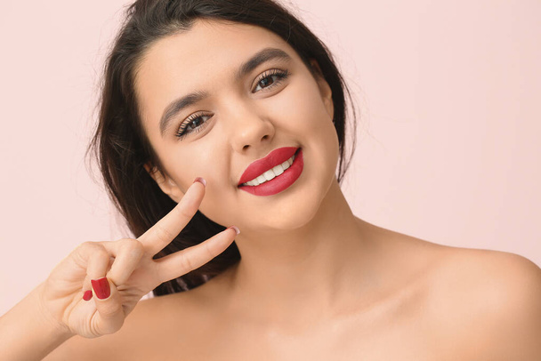 Nuori nainen punainen huulipuna osoittaa voiton ele vaaleanpunainen tausta, lähikuva - Valokuva, kuva