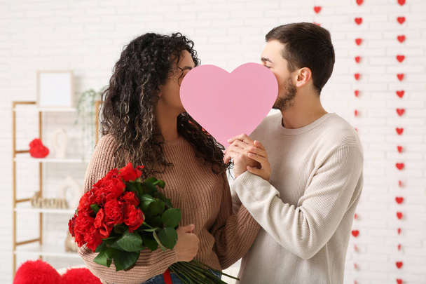 Junges Paar mit Rosenblüten und Papierherz zum Valentinstag zu Hause - Foto, Bild
