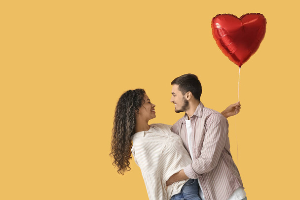 Young couple with air balloon in shape of heart for Valentine's day on yellow background - Photo, Image