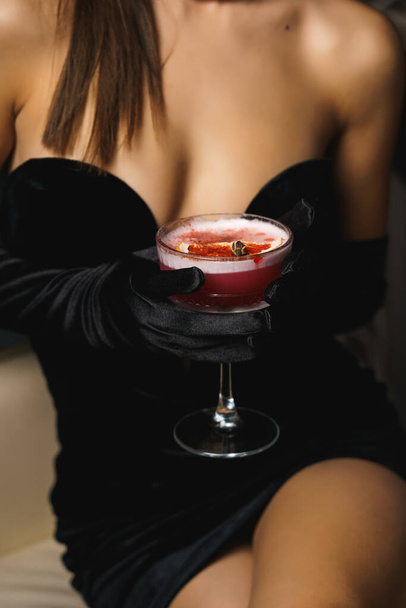 Femme sexy dans une robe noire avec des gants et des lèvres rouges tient un cocktail.Nightlife concept - Photo, image