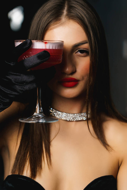 Mujer sexy en un vestido negro con guantes y labios rojos sostiene un concepto cocktail.Nightlife - Foto, Imagen