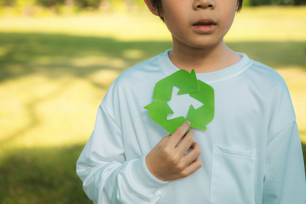 Wesoły młody azjatycki chłopiec posiadający symbol recyklingu w świetle dziennym naturalny zielony park promujący recykling odpadów, ograniczający i ponownie wykorzystujący zachętę do ekologicznej zrównoważonej świadomości dla przyszłych pokoleń. Żywica - Zdjęcie, obraz