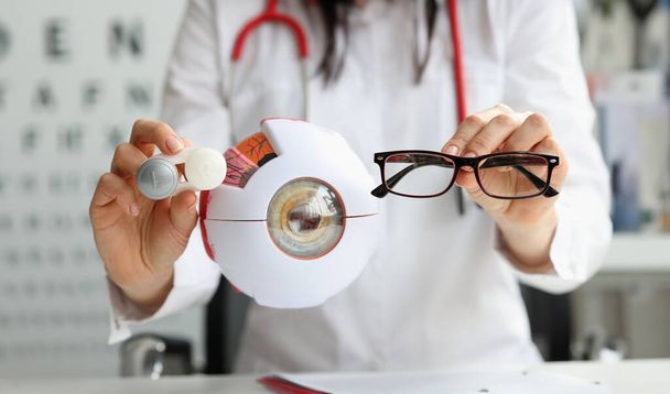Médico oftalmólogo sosteniendo anteojos y lentes cerca del modelo artificial de primer plano. Concepto de corrección de visión - Foto, imagen