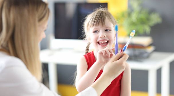 Holčička vybírá zubní kartáček v ordinaci zubařů. Denní ústní péče o děti koncept - Fotografie, Obrázek