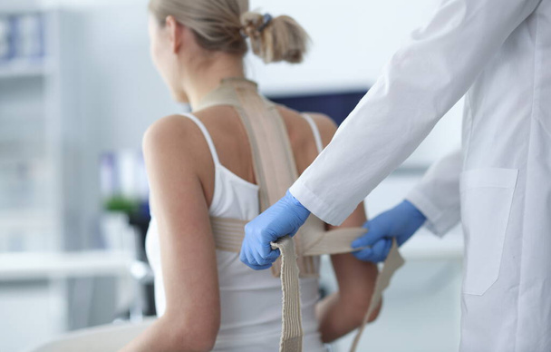 Doutor colocando espartilho na parte de trás do paciente feminino close-up. Conceito de tratamento da curvatura espinhal - Foto, Imagem